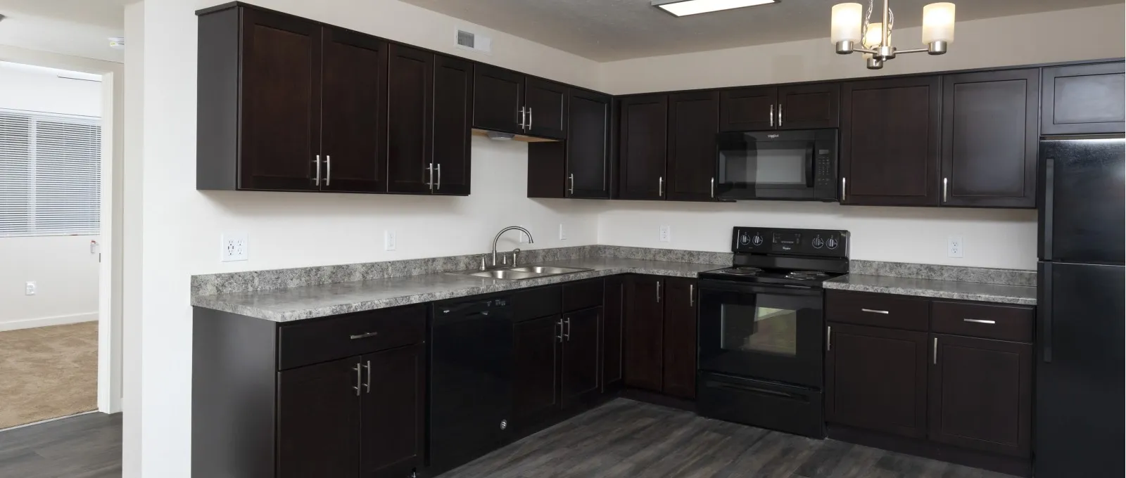 Modern kitchen with dark wood cabinets, marble countertops, and stainless steel appliances. Grey flooring adds to the sleek, minimalist design.