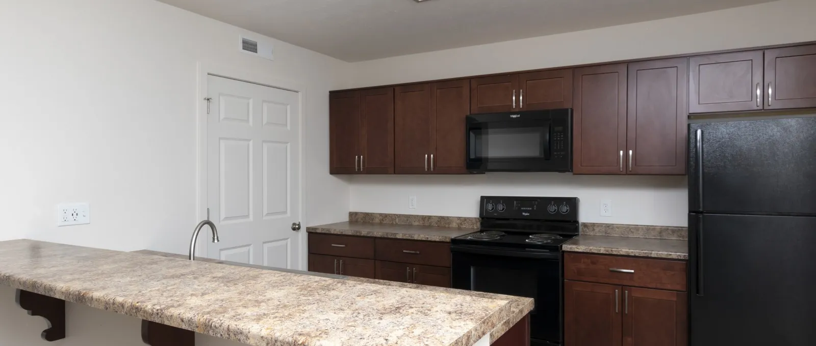 A modern kitchen with dark wood cabinets, a marble countertop, and black appliances, creating a clean and warm atmosphere.