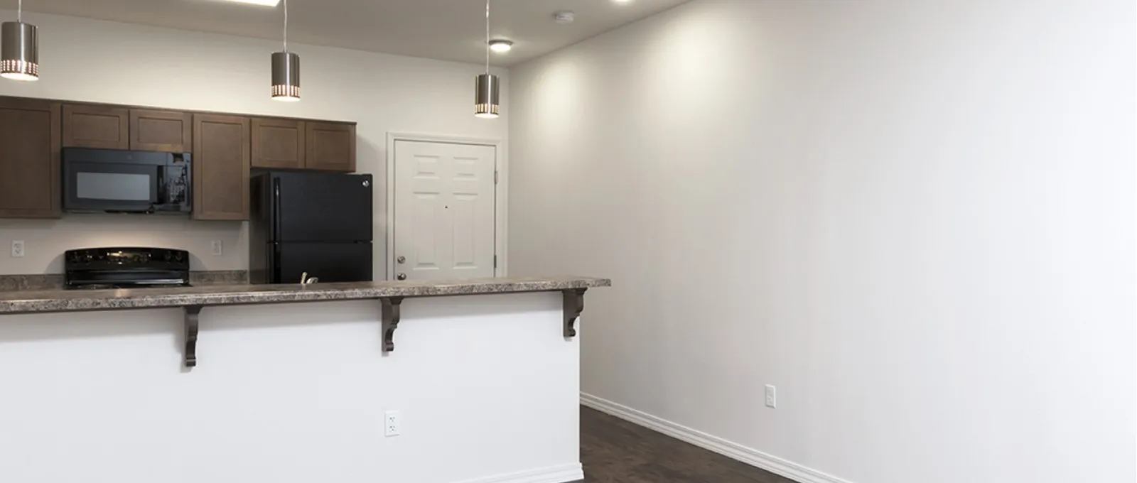 Kitchen bar area at Market Street Apartments with pendant lighting, dark countertops, and white walls accented by recessed lighting and dark plank-style floors.