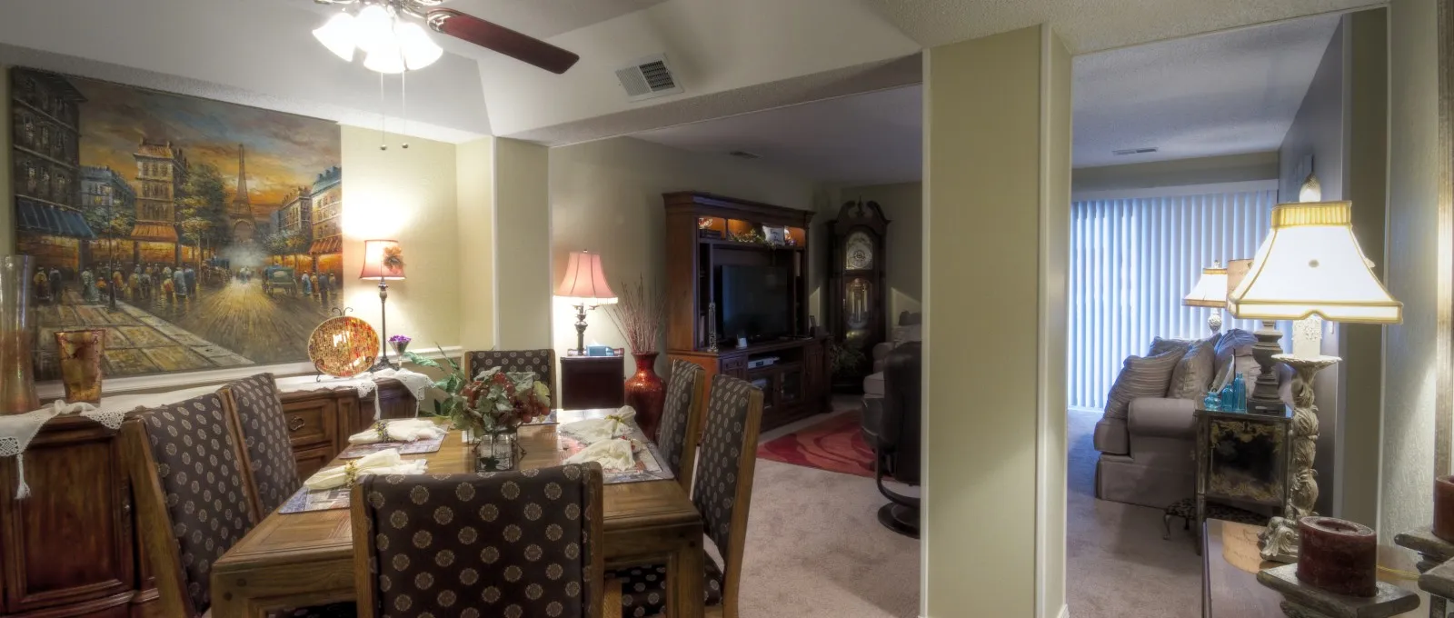 Cozy living and dining area with warm lighting. Includes a wooden dining table, chairs with patterned upholstery, a TV console, and a couch by sliding doors.