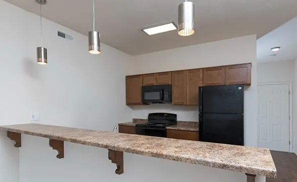 Modern kitchen with dark appliances, wood cabinetry, and bar seating at Market Street Apartments in Springfield, MO.