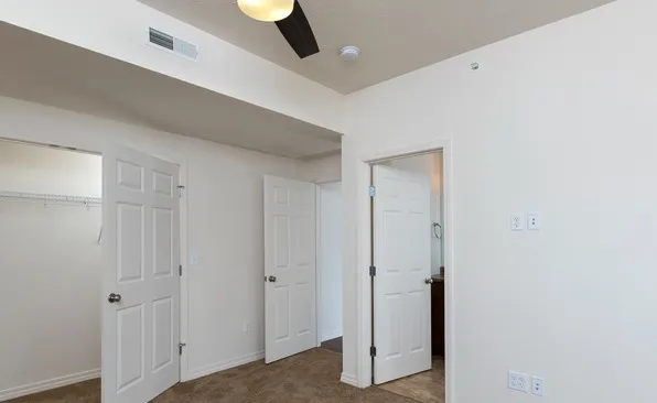 Carpeted bedroom with ceiling fan and ensuite bathroom access, perfect for comfortable apartment living.