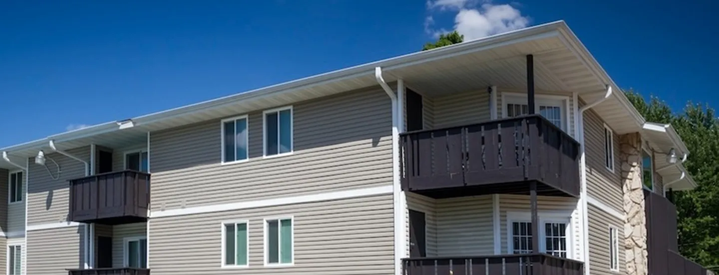 Modern two-story apartment building with gray siding, large windows, and a black balcony under a clear blue sky.