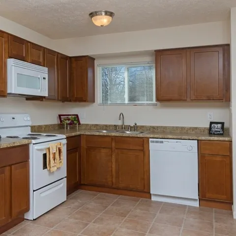 U-shaped kitchen featuring wood cabinets, white appliances, dishwasher, microwave, and large window above the sink—designed for everyday function and comfort.