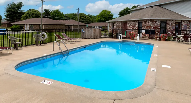 Outdoor pool at Grandview Village Apartments bordered by black fencing, with nearby red brick office and patio seating area.