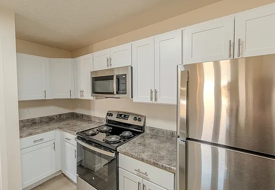 Close-up of updated kitchen cabinetry and countertops with stainless range, microwave, and refrigerator in Battlefield, MO apartment.