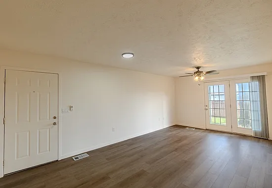 Spacious living room at Huntley Ridge Apartments in Battlefield MO, featuring wood-style flooring, neutral walls, ceiling fan, and French doors leading to a private backyard&mdash;perfect for comfortable and pet-friendly living.