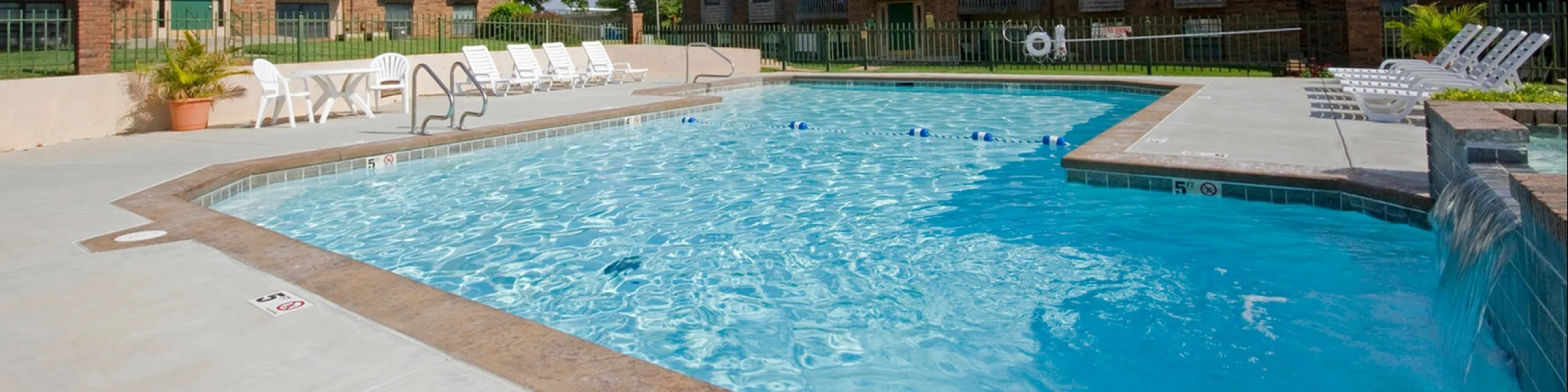 Inviting apartment complex featuring a shimmering swimming pool surrounded by sun loungers and lush landscaping.