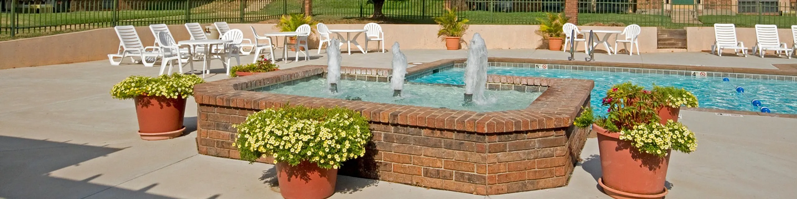 Charming apartment complex showcasing a sparkling swimming pool with fountains, surrounded by lush greenery and inviting lounge chairs.