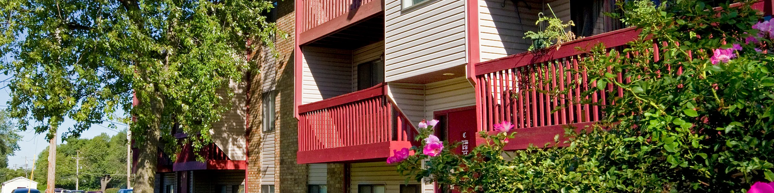 Charming apartment complex with vibrant red balconies, nestled among lush greenery and colorful flowers, perfect for comfortable living.
