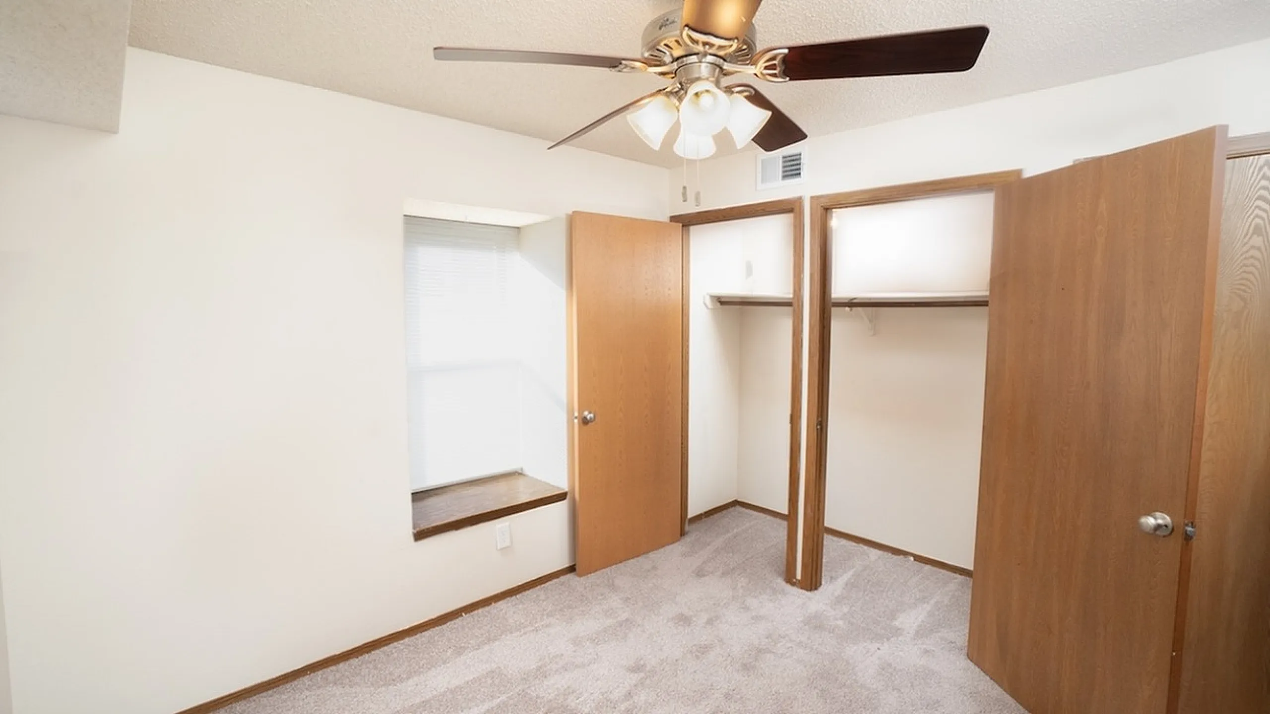 Bright, airy bedroom with plush carpeting, built-in closet space, and a stylish ceiling fan for modern comfort.