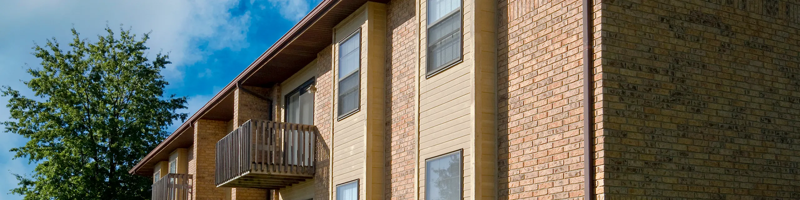 Charming brick apartment building with private balconies and lush green lawn under a clear blue sky.