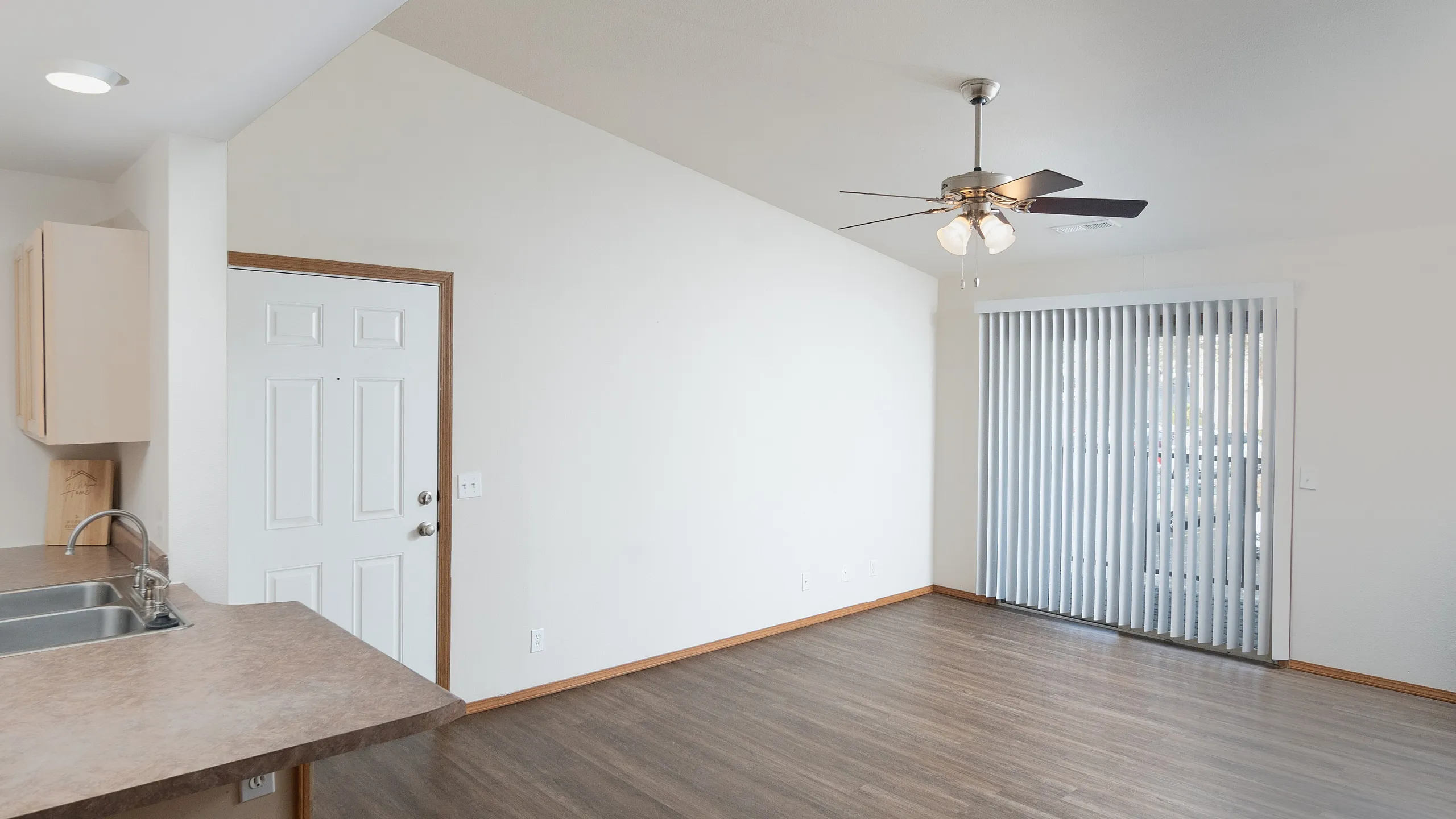 Bright, open living area with modern ceiling fan and sleek hardwood floors, adjacent to a cozy kitchen space with stylish countertops and a double sink.