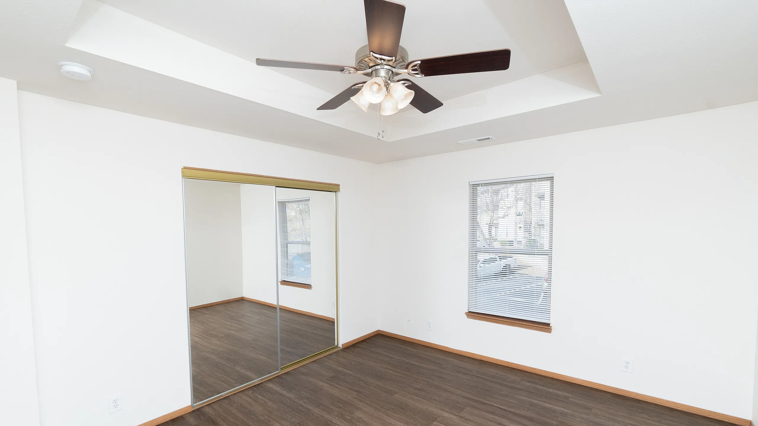 Bright and airy bedroom with elegant wood flooring, a spacious mirrored closet, and a ceiling fan for comfort.