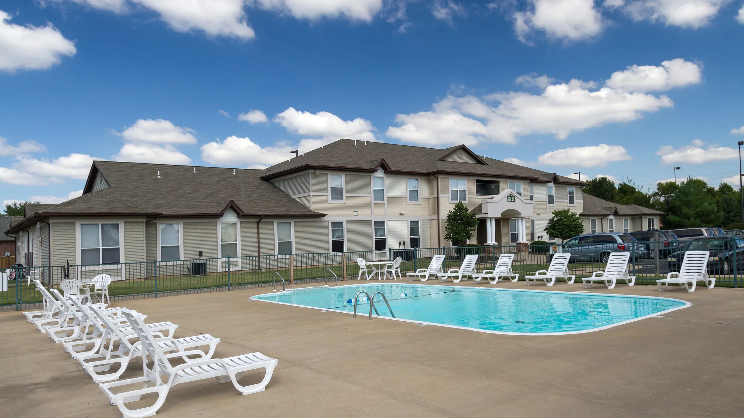 Charming apartment complex with a refreshing outdoor pool, perfect for relaxation and leisure under a bright blue sky with fluffy clouds.