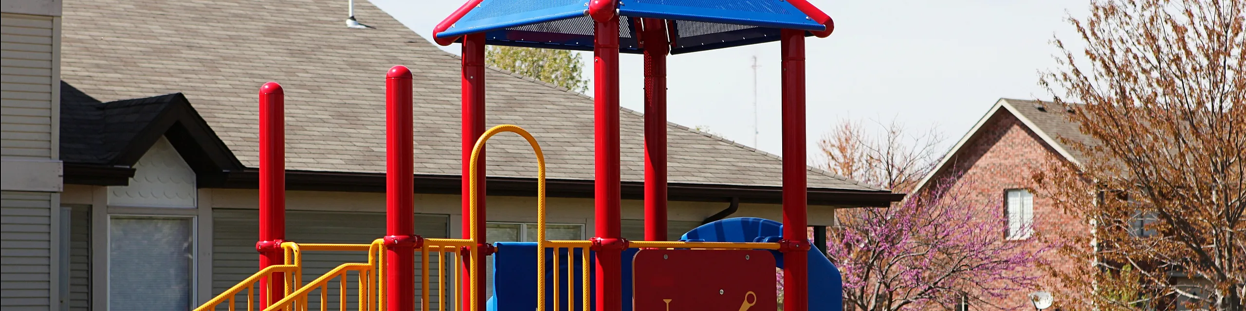 Charming residential playground with vibrant red, blue, and yellow play structures, set against a peaceful suburban backdrop.