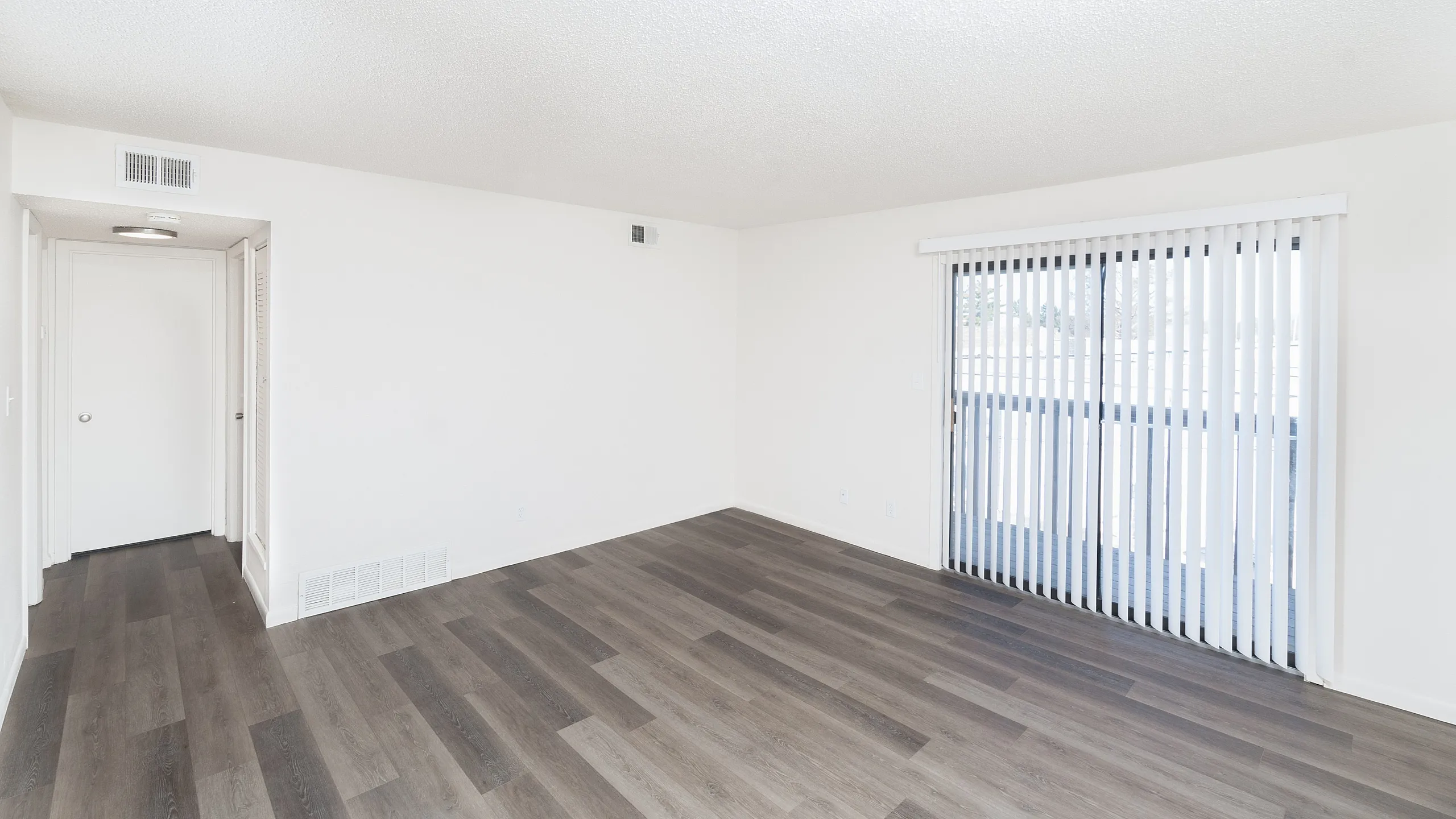 Bright, expansive living room with sleek hardwood floors and large sliding glass doors leading to a balcony.