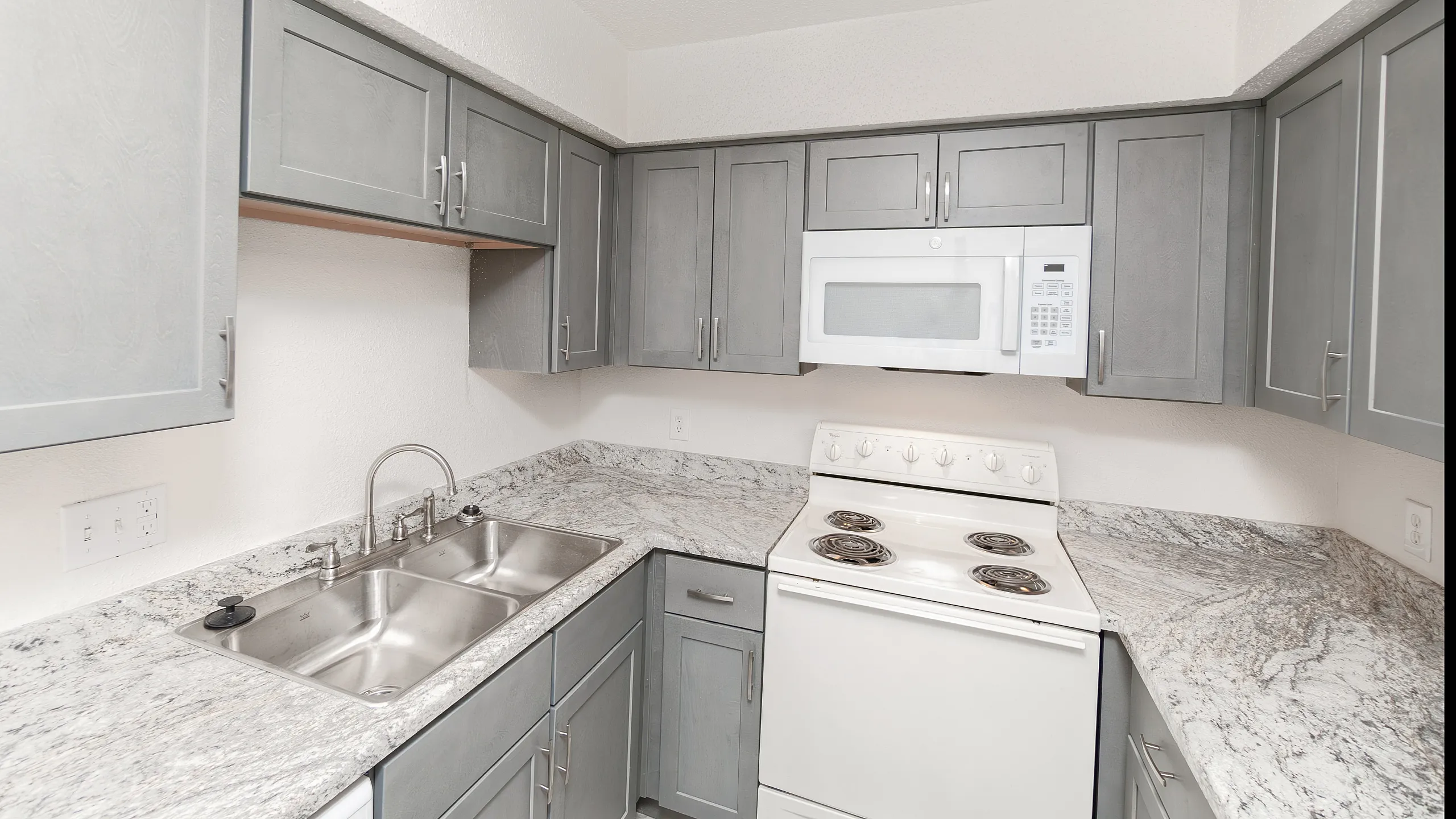 Modern kitchen with sleek gray cabinetry, elegant marble countertops, and pristine stainless steel sink.