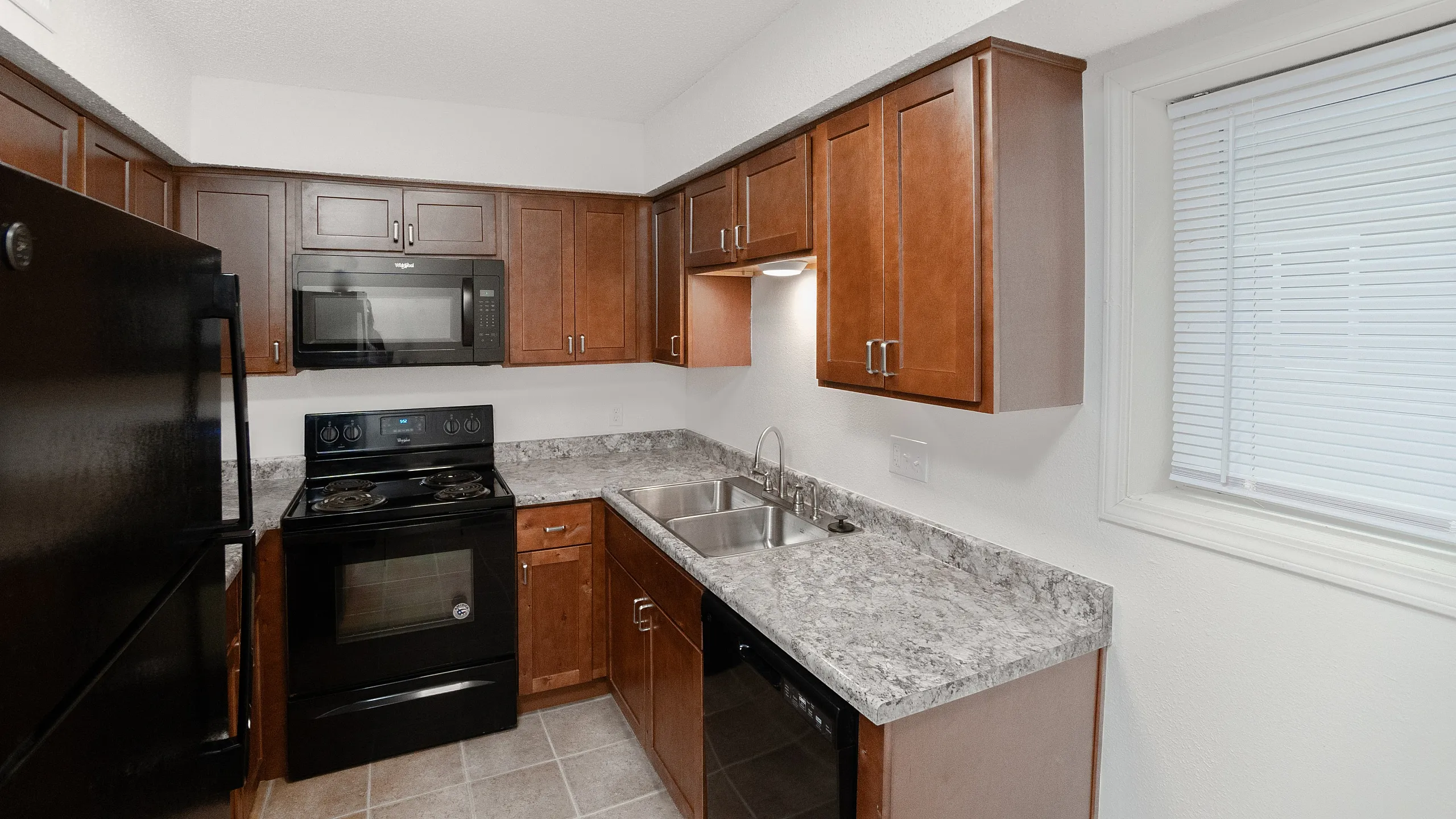 Modern kitchen with sleek black appliances, elegant wood cabinetry, and a polished granite countertop, offering ample cooking space and stylish design.