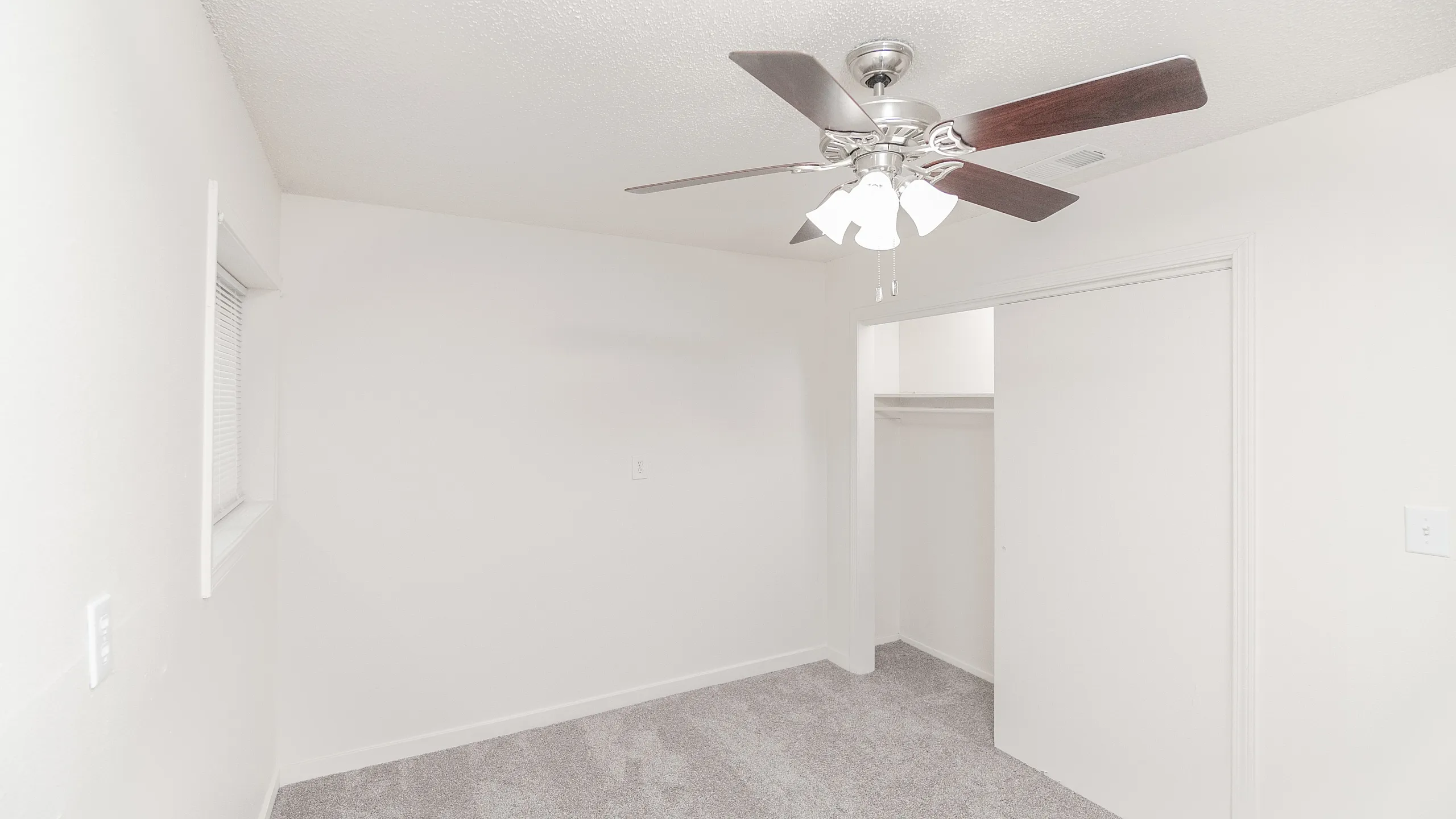 Bright, modern bedroom with fresh carpet, white walls, and a ceiling fan, featuring a spacious closet.
