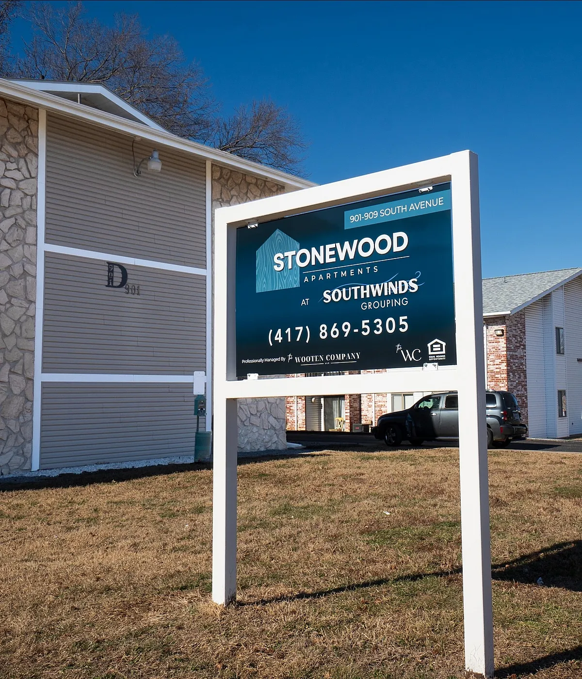 Inviting Stonewood Apartments sign with a charming building exterior and ample parking, set against a clear blue sky.