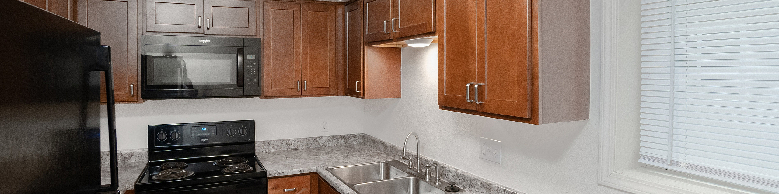 Modern kitchen with sleek black appliances, elegant wood cabinetry, and polished granite countertops.