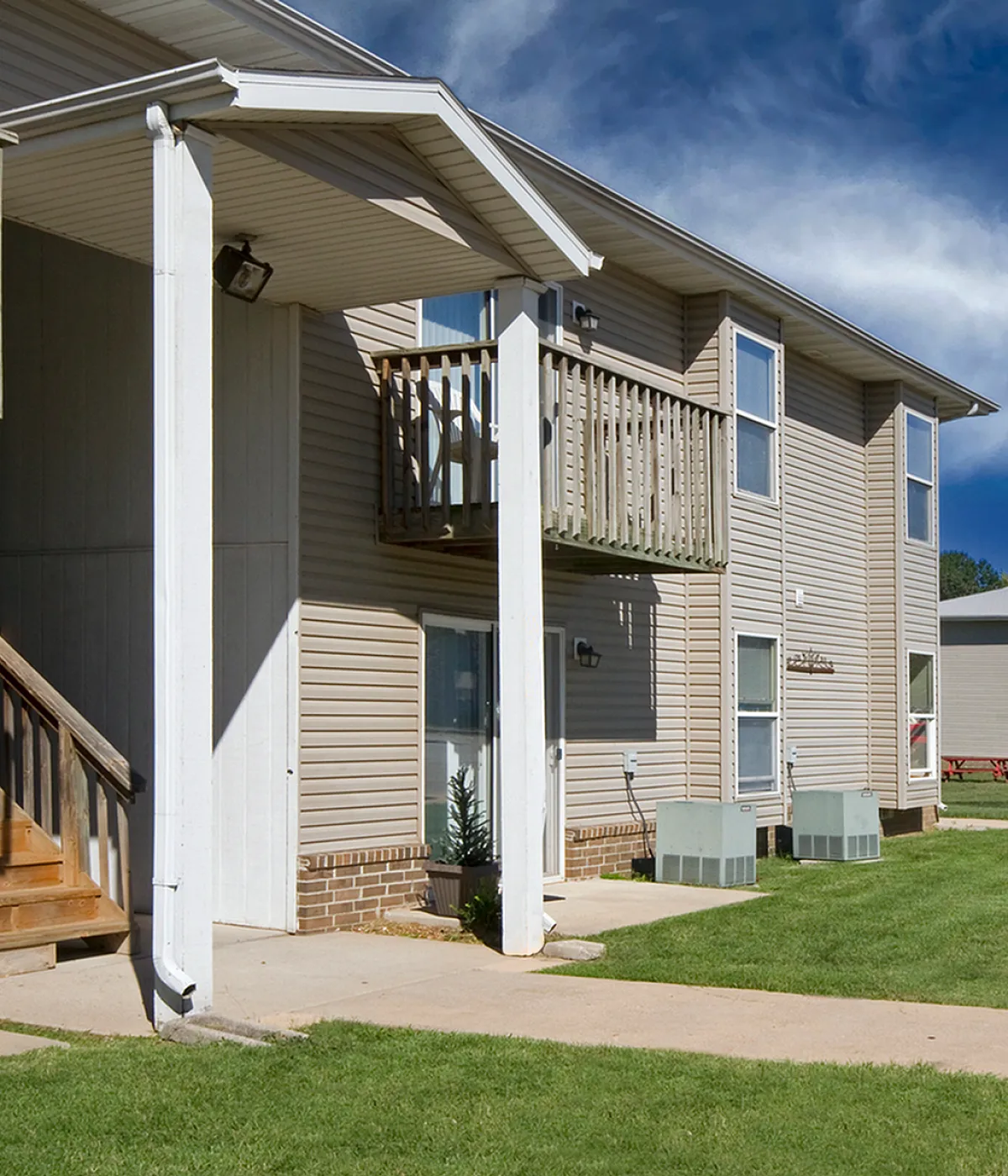 Charming apartment complex exterior featuring modern balconies, lush green lawns, and a bright blue sky backdrop.
