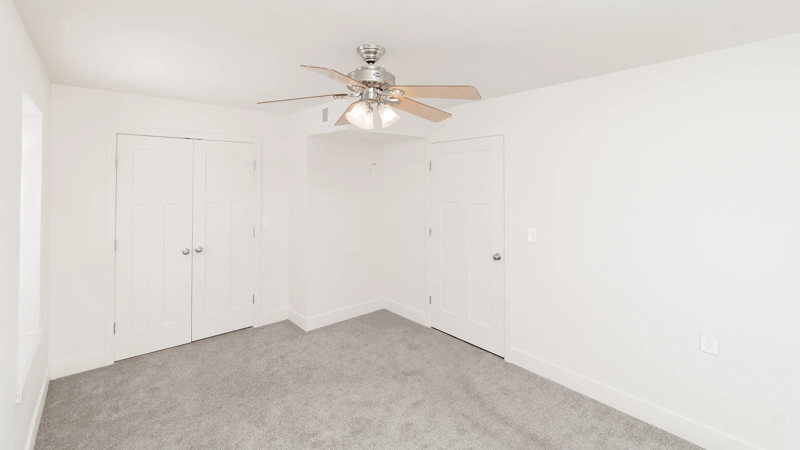 Bright and inviting bedroom featuring plush carpeting, a stylish ceiling fan, and ample closet space.