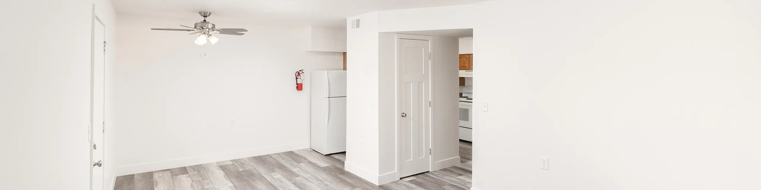 Bright and airy apartment interior showcasing elegant wood flooring, a contemporary ceiling fan, and a cozy kitchen area.