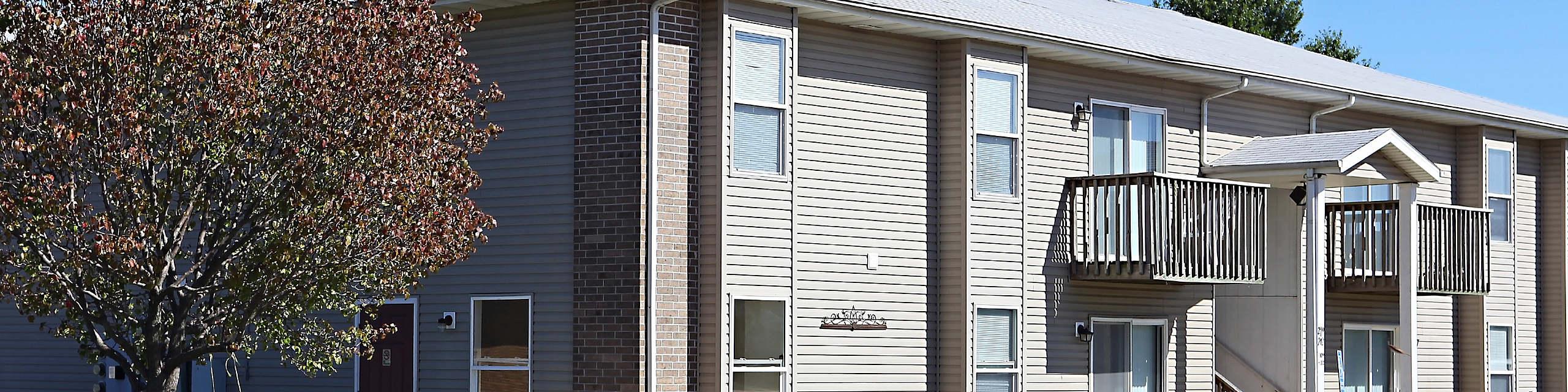 Charming two-story apartment building with a brick facade, cozy balconies, and lush green lawn on a sunny day.