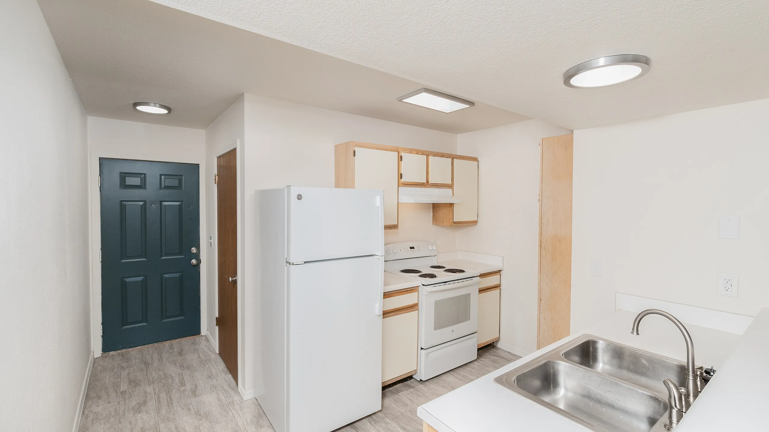 Kitchen with white appliances, light cabinetry, breakfast bar, wood-look flooring and entry door view