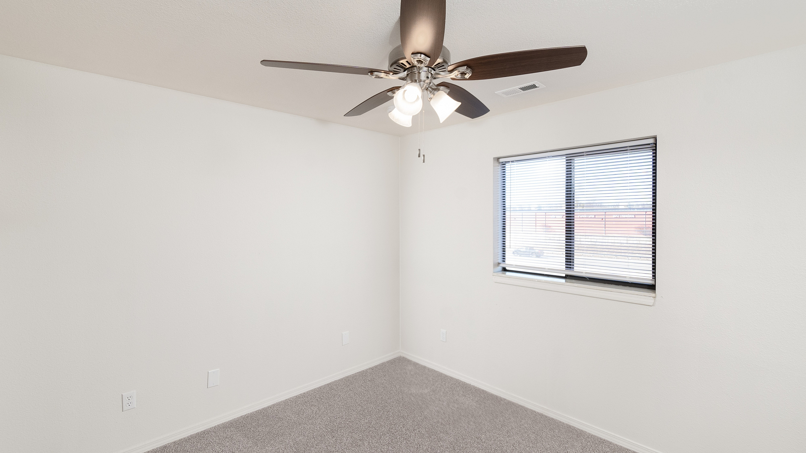 Bright and airy room with fresh white walls, plush carpet, and a sleek ceiling fan, offering comfort and style.