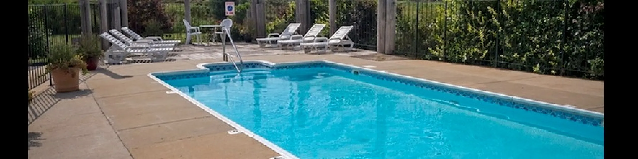 Inviting outdoor swimming pool surrounded by lush greenery and comfortable lounge chairs, perfect for relaxation under the blue sky.