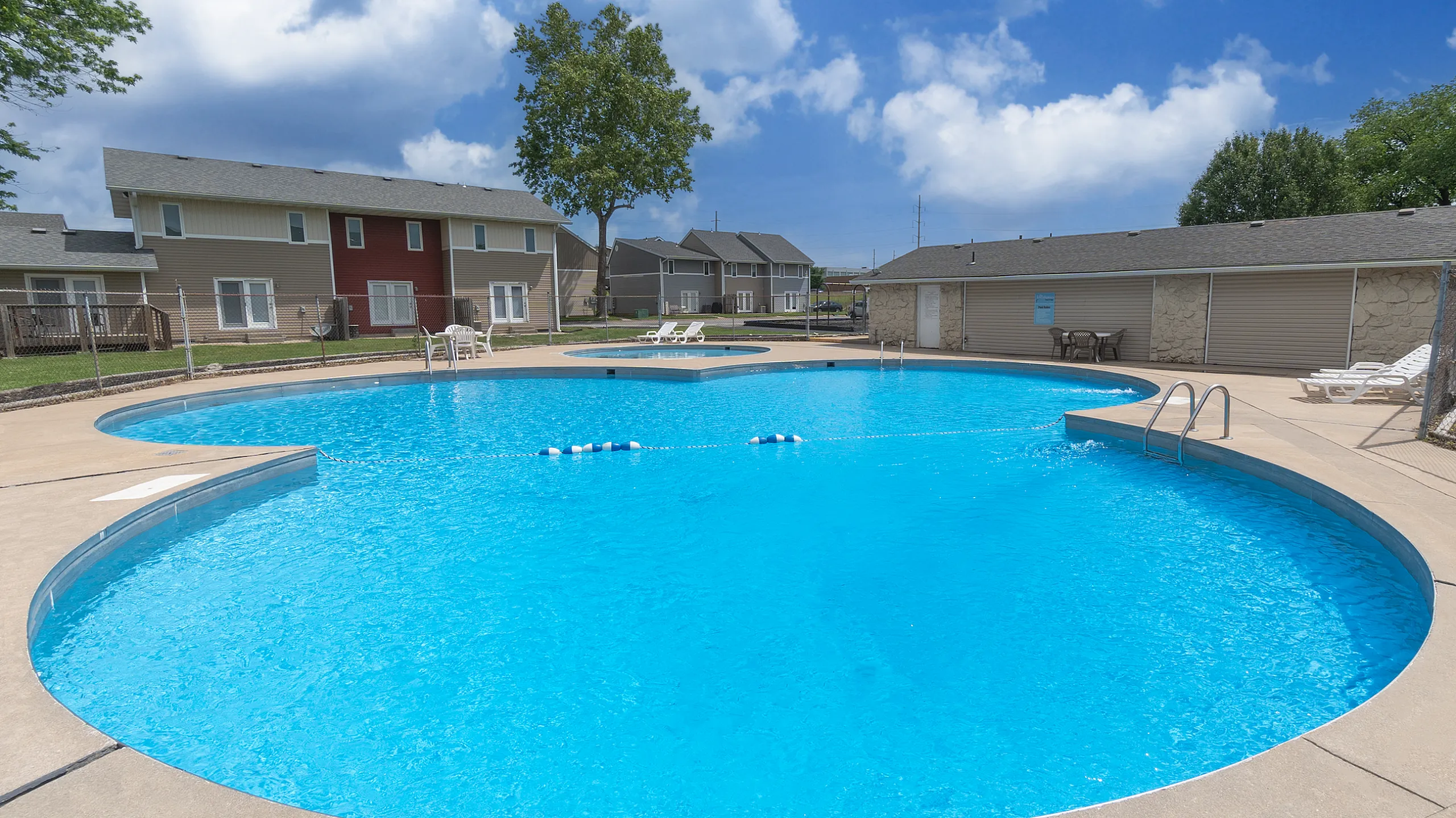 Inviting outdoor pool surrounded by modern townhouses and lush greenery, perfect for relaxing under a bright blue sky.