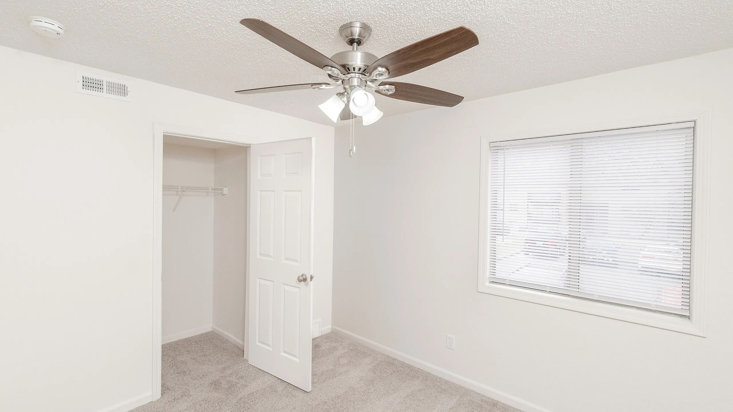 Bright and airy bedroom with plush carpet, modern ceiling fan, and ample natural light from large window; features a spacious walk-in closet.