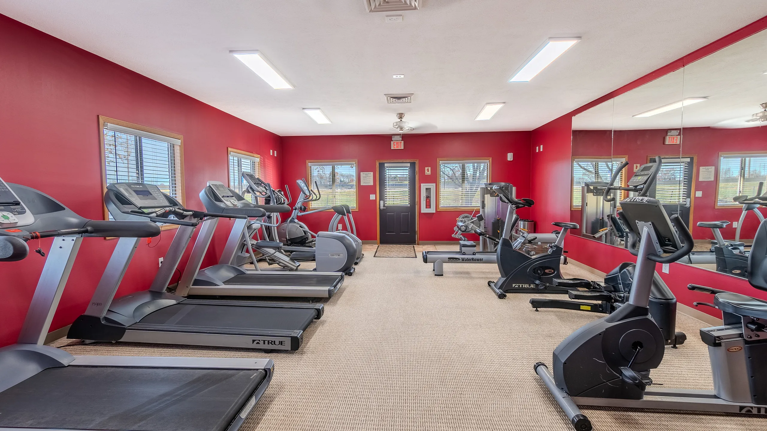 Vibrant gym room with modern cardio equipment including treadmills and stationary bikes, set against bold red walls and expansive mirrors for an invigorating workout experience.