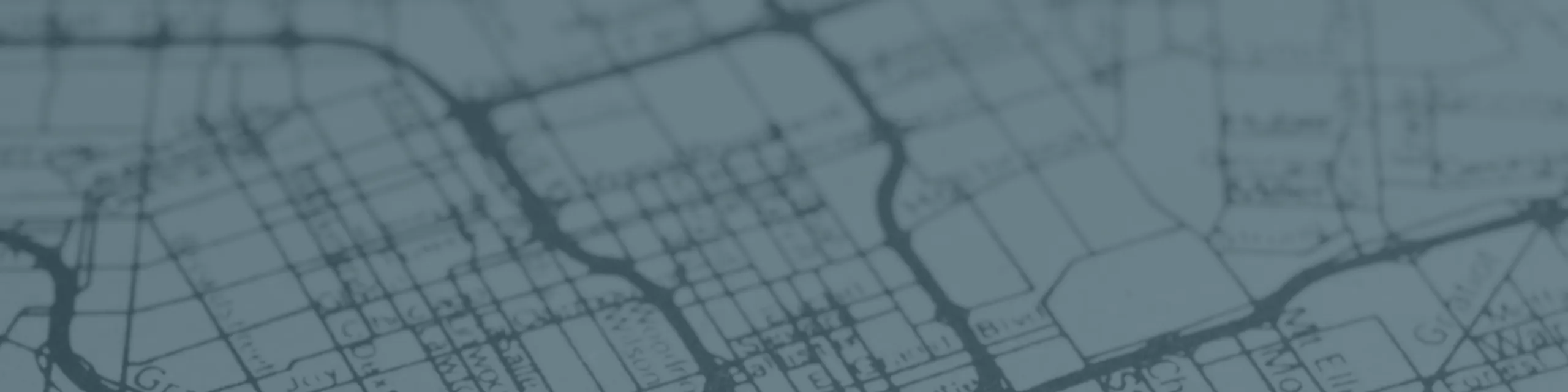 Blurred blue-toned city street map background showing roads and intersections, used as a decorative header for directions or location information.