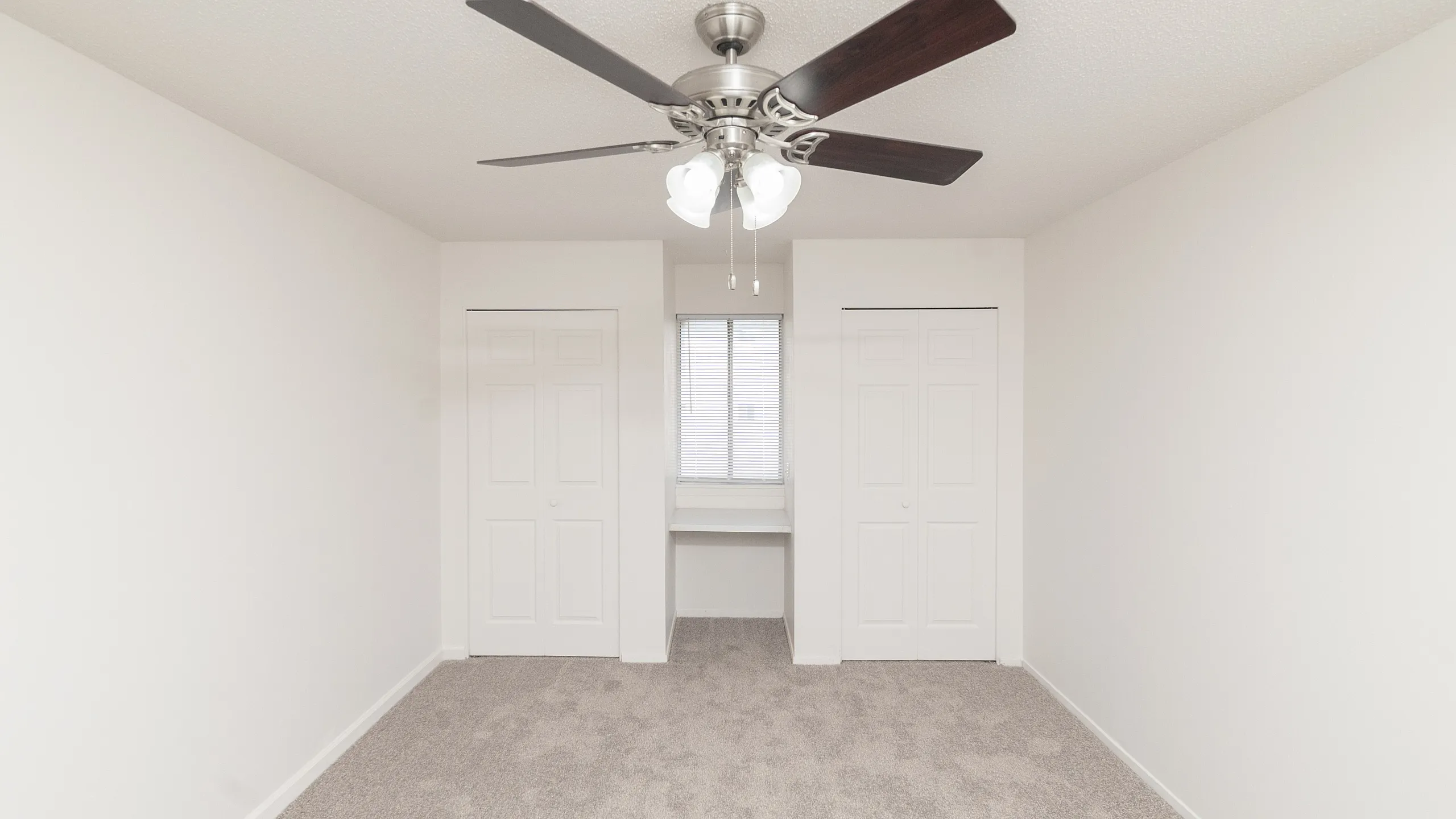 Bright, carpeted room with modern ceiling fan, dual closets, and a cozy nook by the window.