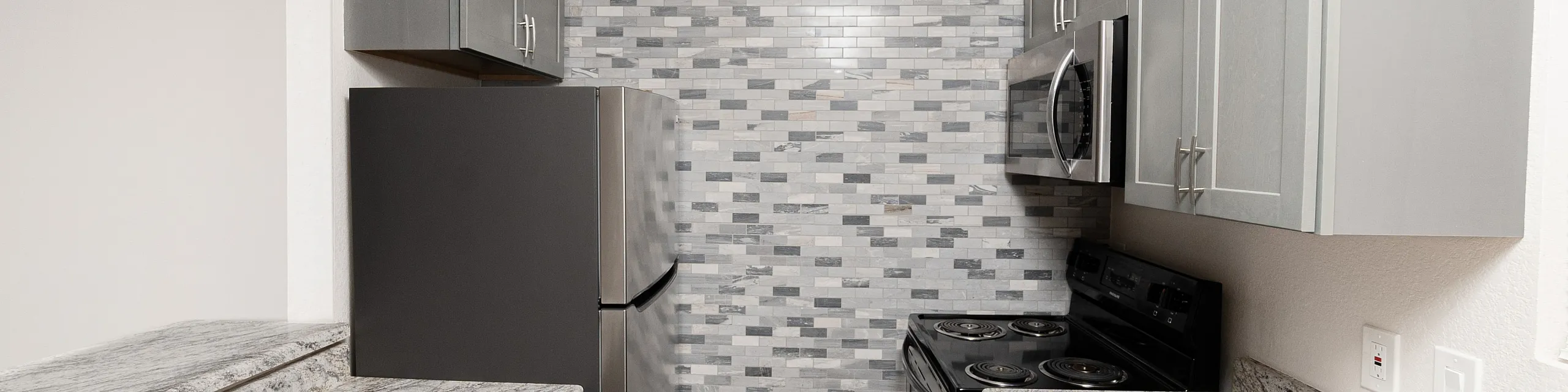 Modern kitchen with sleek gray cabinets, stainless steel appliances, and elegant marble countertops, featuring a stylish tiled backsplash.
