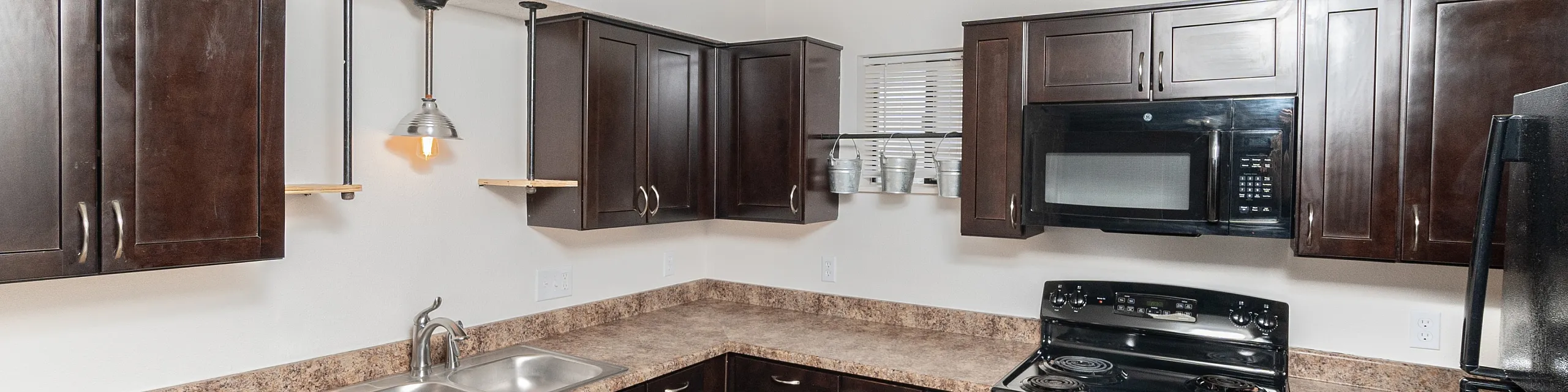 Modern kitchen with sleek dark wood cabinets, stainless steel sink, and elegant lighting, offering a stylish and functional space.