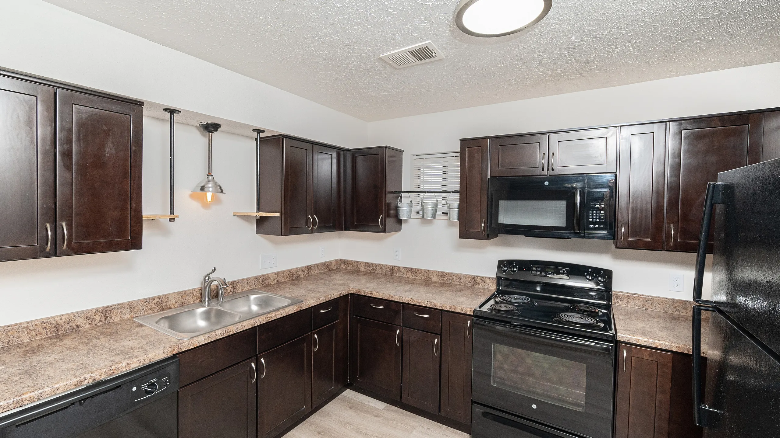 Modern kitchen with sleek dark cabinets, stainless steel sink, and contemporary lighting, perfect for culinary enthusiasts.