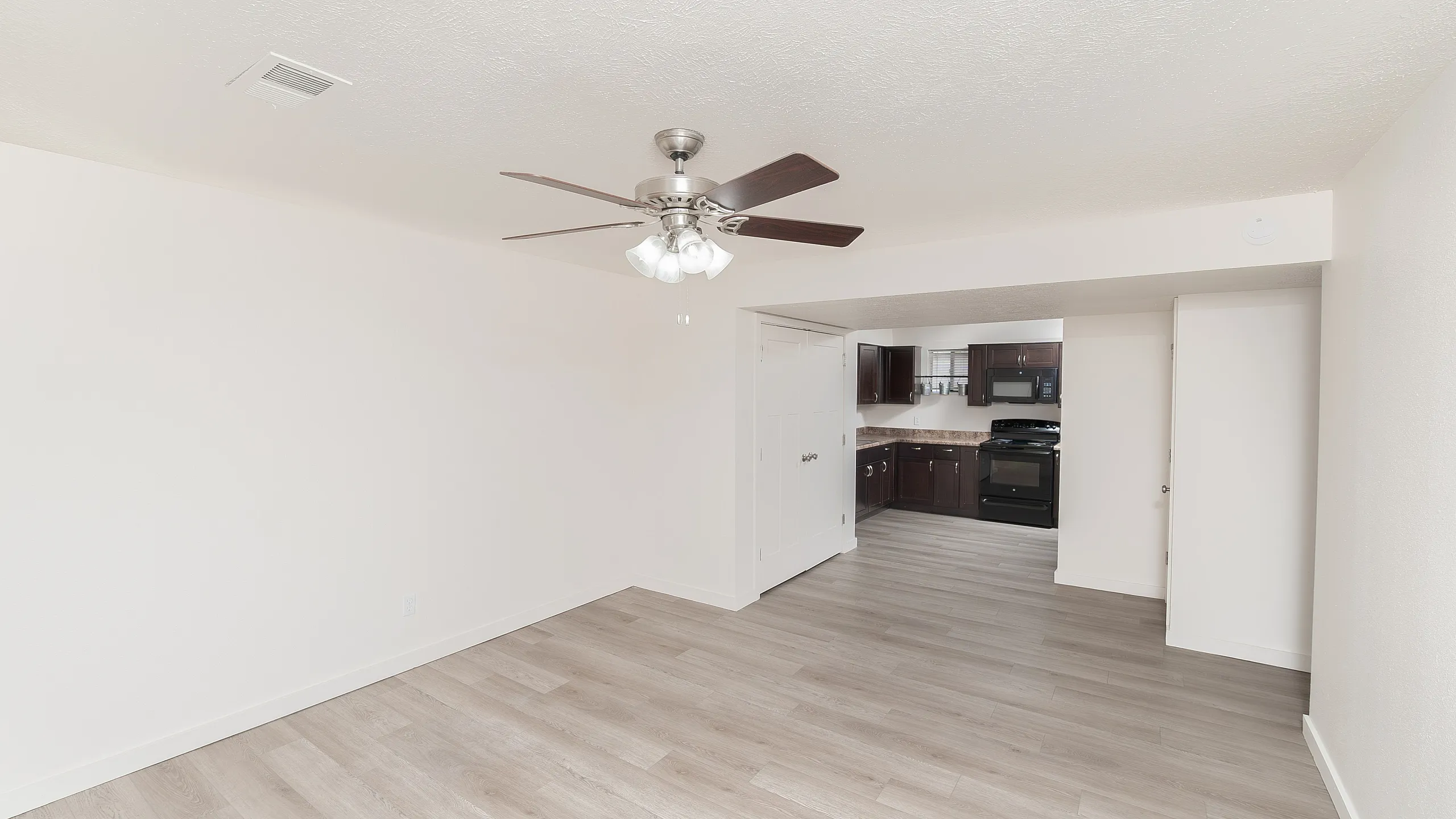 Bright and airy open-concept apartment with sleek wood flooring, modern ceiling fan, and a stylish kitchen with dark cabinetry.
