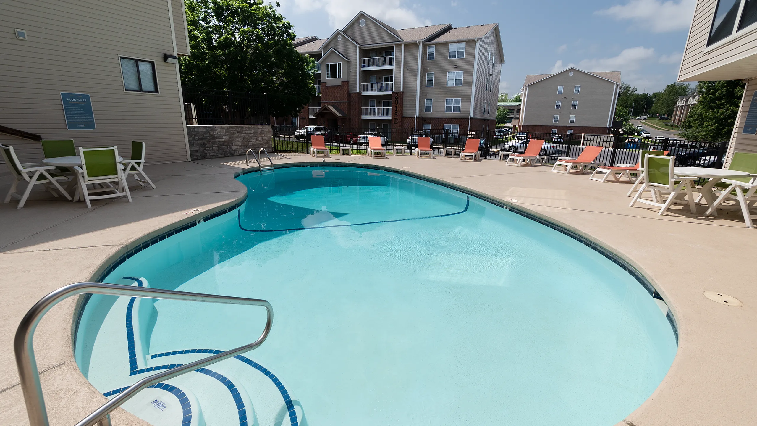 Inviting apartment community pool with sun loungers and patio seating, surrounded by modern residential buildings.