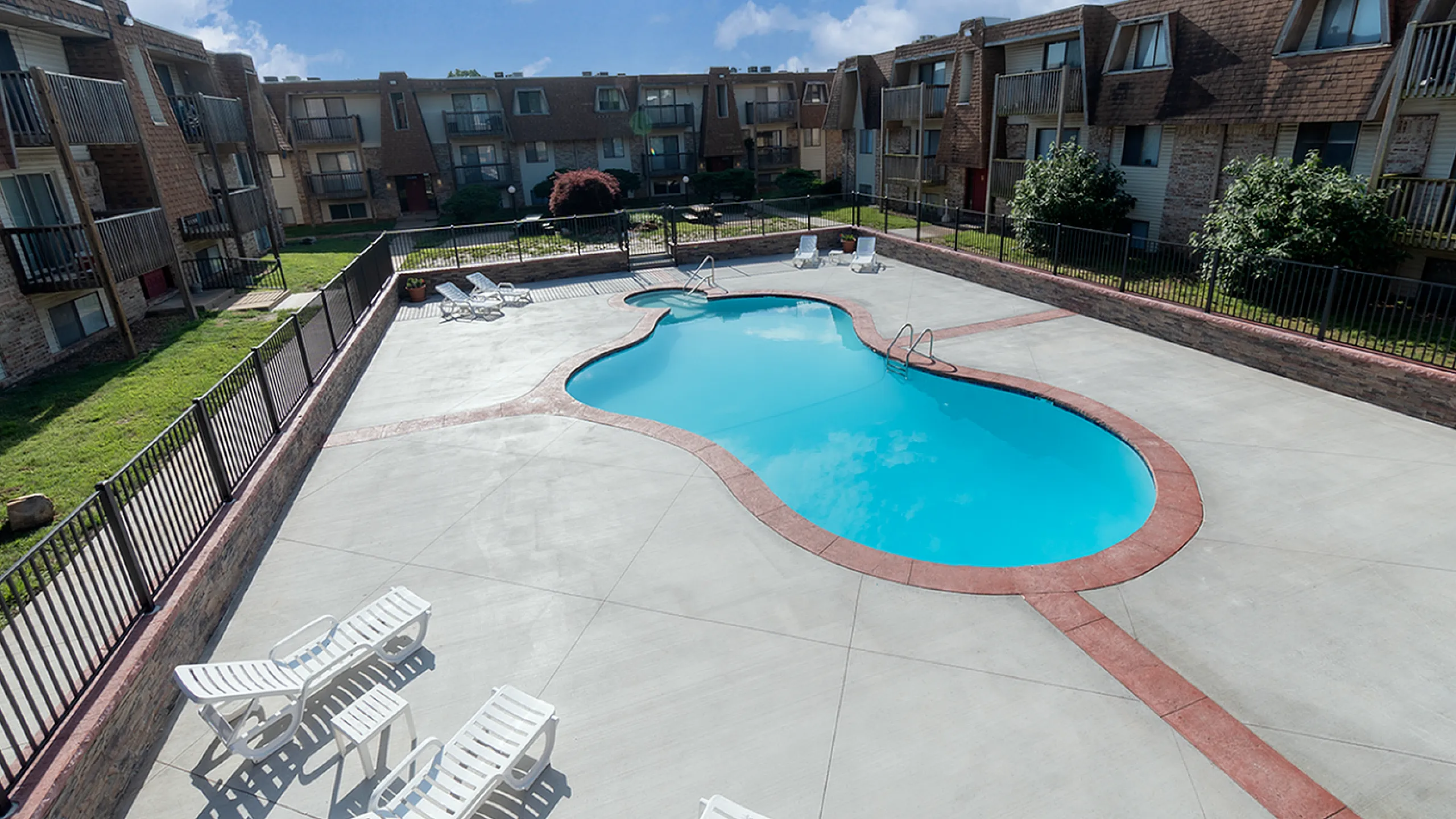 Inviting apartment complex with a sparkling outdoor pool, sun-kissed deck, and charming balconies overlooking the serene courtyard.