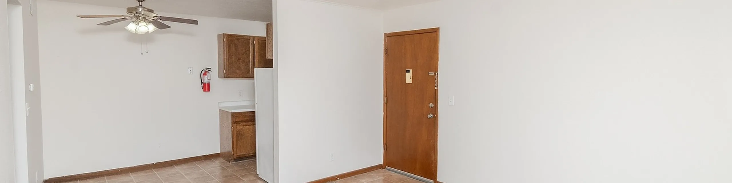 Bright apartment interior with open living and dining area, featuring a ceiling fan and cozy carpet flooring adjacent to a kitchen with modern cabinetry.