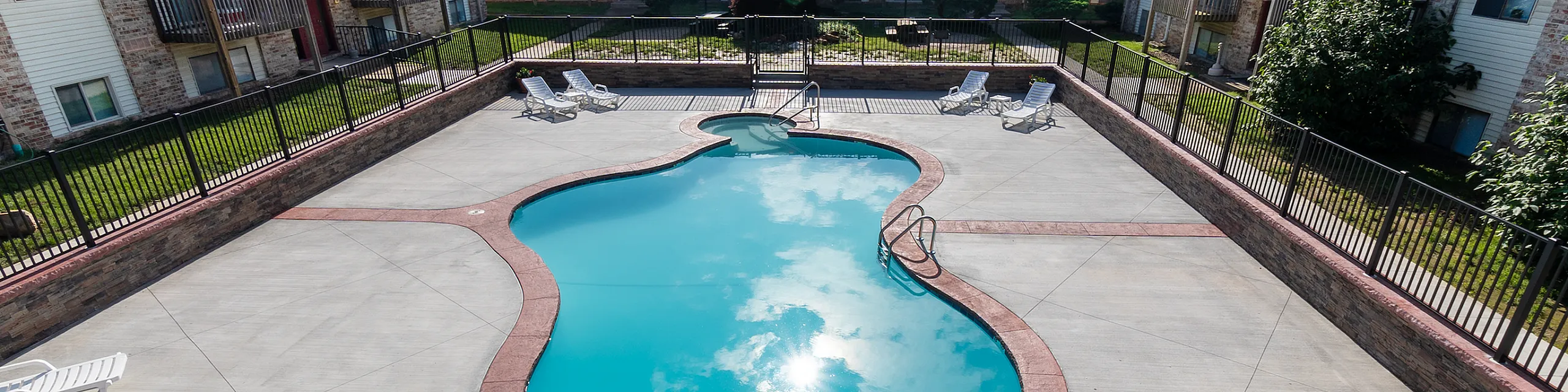 Inviting outdoor swimming pool area surrounded by modern apartment buildings, featuring cozy lounge chairs and a tranquil atmosphere.