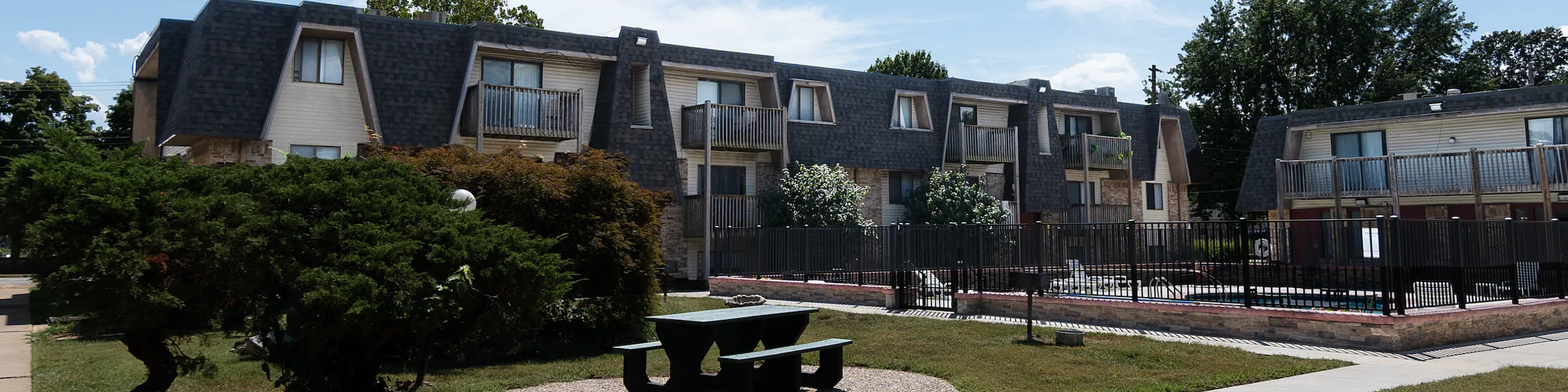 Charming apartment complex with modern architecture, surrounded by lush greenery and featuring a serene outdoor pool area.