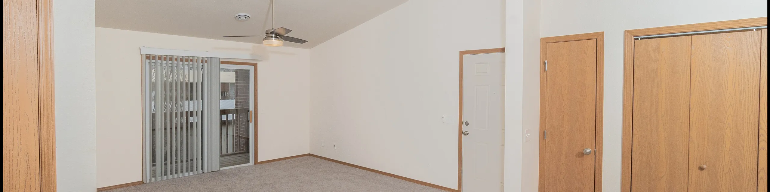 Inviting apartment interior with plush carpet flooring, modern ceiling fan, and glass sliding doors leading to a balcony. Features elegant lighting and ample closet space for a sophisticated living experience.