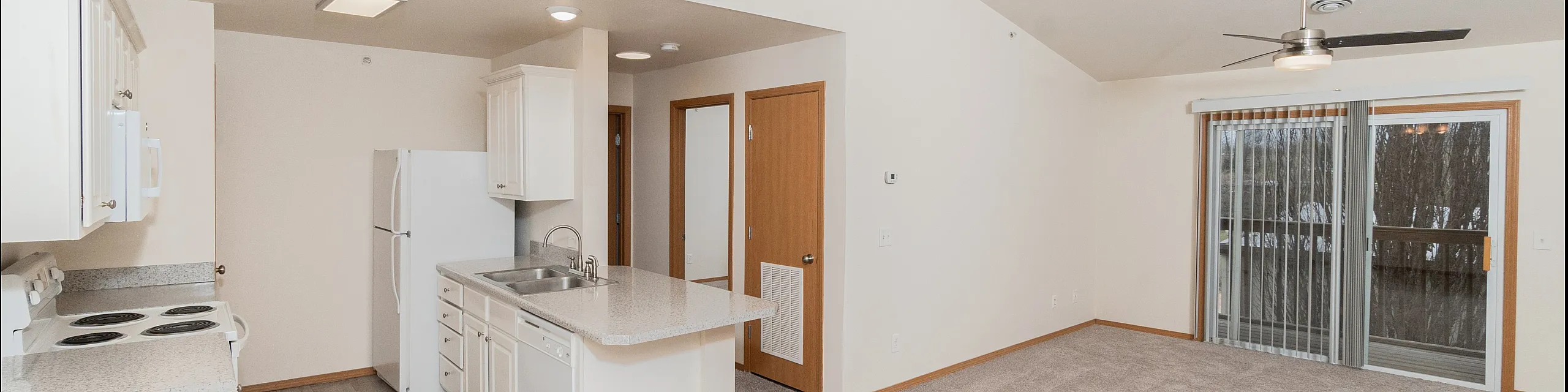 Bright open-concept apartment featuring a modern kitchen with white cabinetry and an inviting living area with sliding glass doors leading to a balcony.