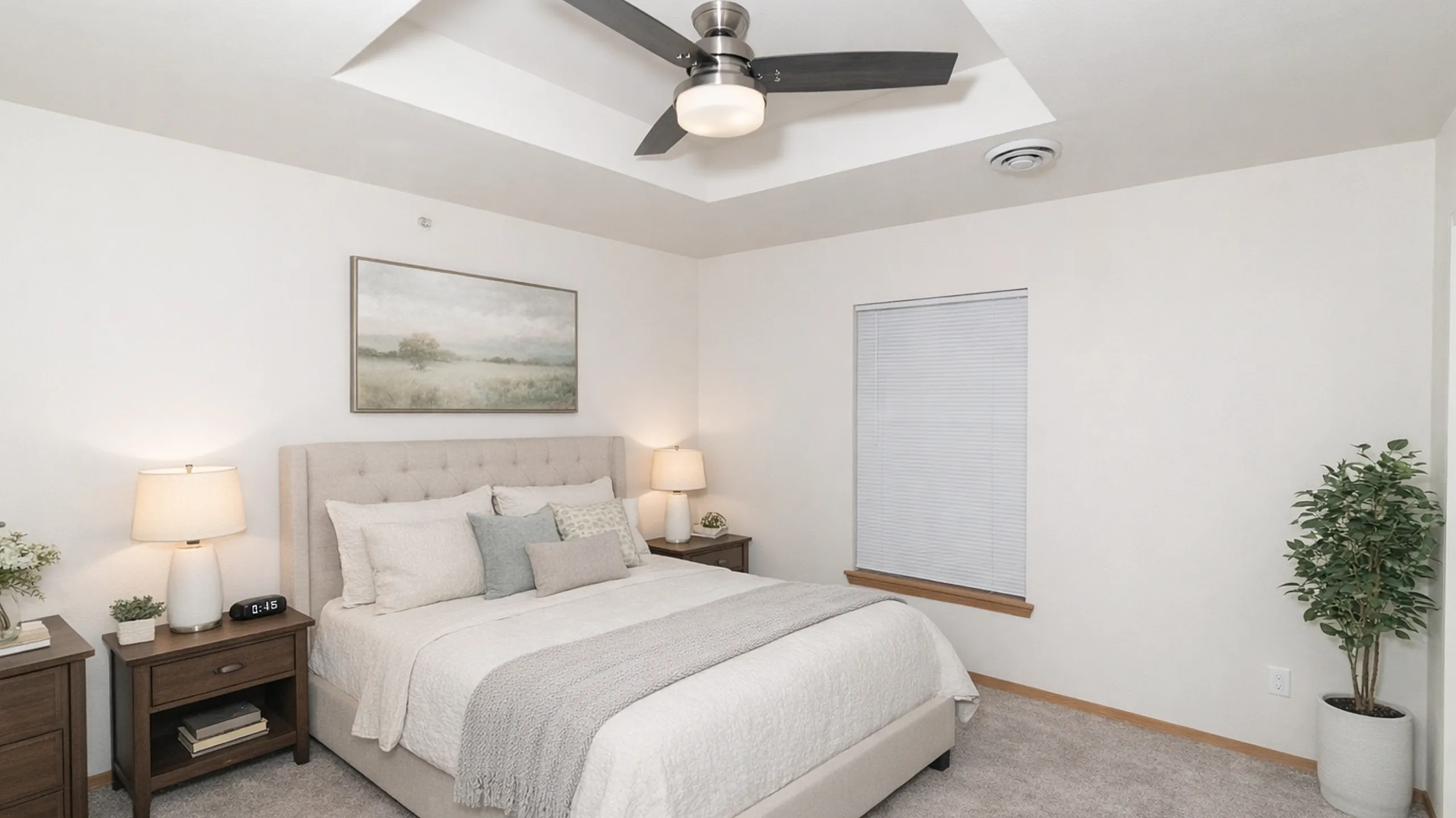 Inviting bedroom with plush carpeting, stylish ceiling fan, and cozy double bed adorned with elegant cushions, complemented by soft lighting and tasteful decor.
